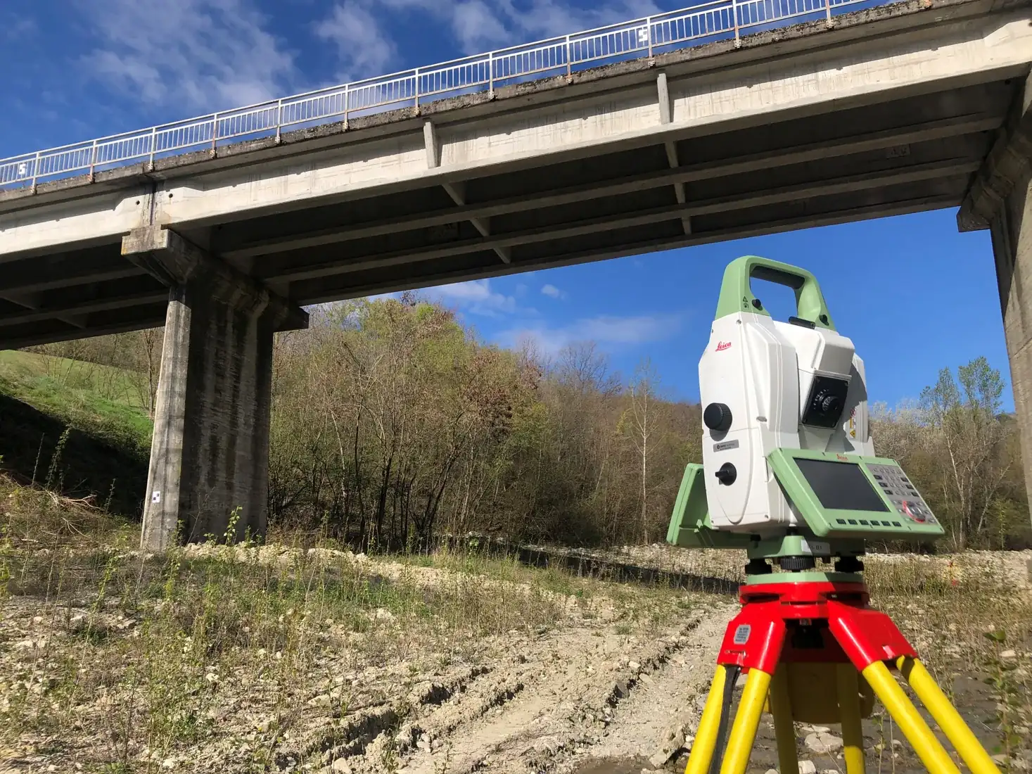 Estação total sobre tripé em levantamento topográfico junto a uma estrutura de concreto